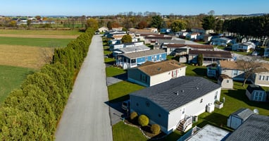 An aerial view shows a community of mobile homes. They are surrounded by farm fields and mature trees.