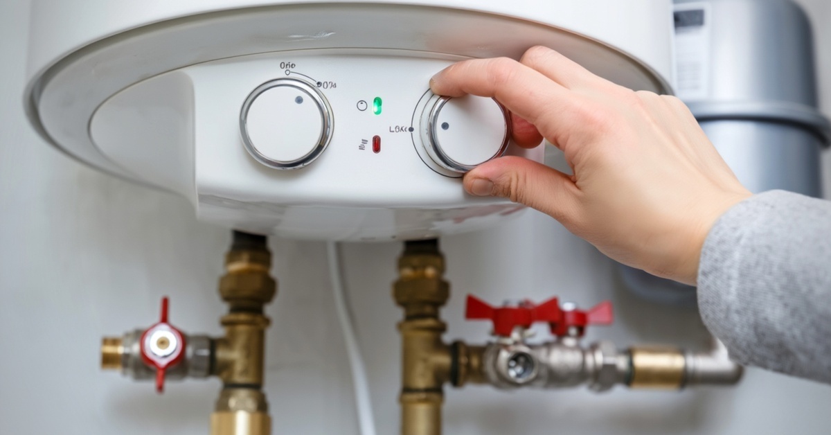A close-up view shows a person adjusting one of two white knobs on a white water heater that is mounted on a wall.