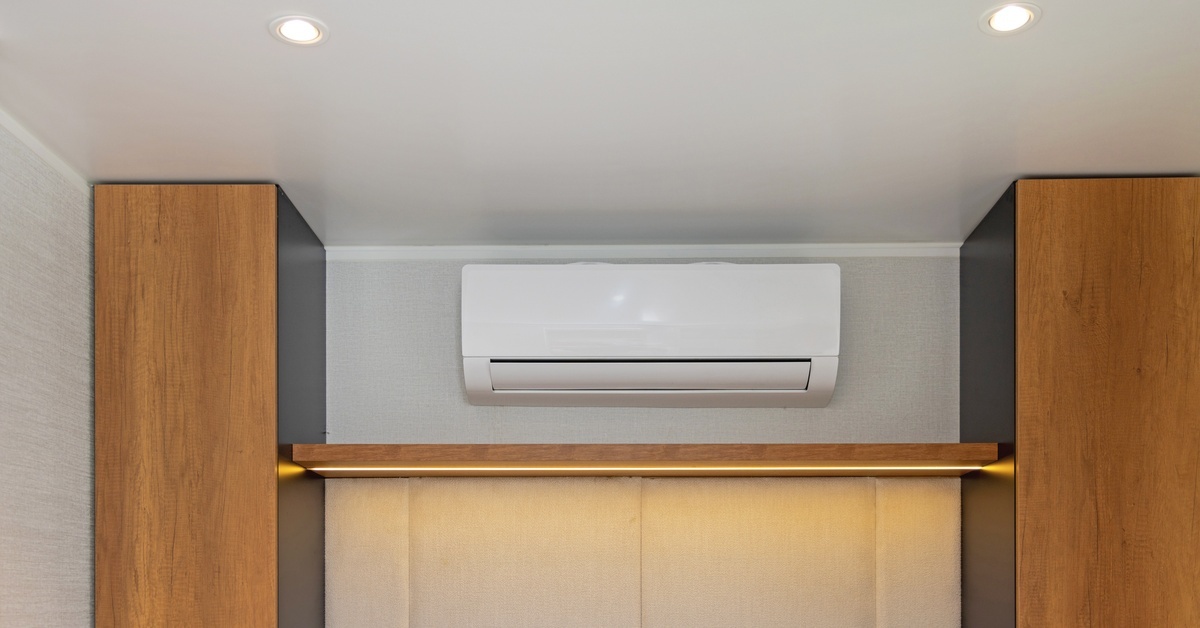 A white ductless air conditioner sits on the wall of a home. Two wooden storage units sit beside the AC unit.