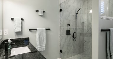 A bathroom features a sink with black countertops, a walk-in shower, black fixtures, and a gray-tiled floor.