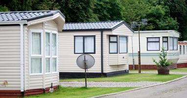 Three manufactured homes sitting beside one another with pavement between each one. One home has a satellite dish on the lawn.